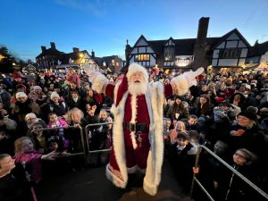Father Christmas holding his hands up like a rock star with his back to the crowds at Knowle Christmas Light Switch on