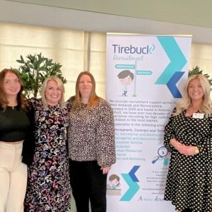 Some of the Tirebuck team standing arm in arm next to a banner advertising Tirebuck services with Emily Tirebuck standing on the other side of the banner