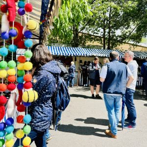 A market stall selling woollen craft decorations is on the left with shoppers browsing market stalls