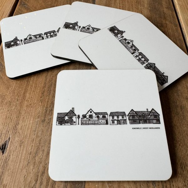 Four coasters set on a wooden table. The identical white coasters have black line drawings of distinctive buildings in Knowle