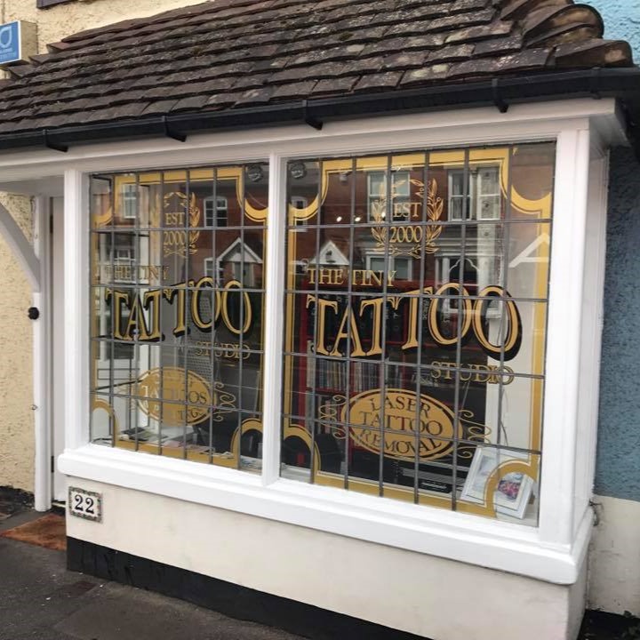 The shop window of The Tiny Tattoo Studio in Knowle featuring a white window frame and gold lettering of the name of the shop