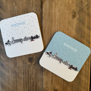 A set of two drinks coasters with a Christmas theme. Snow is falling and a car is driving down the High Street with a Christmas tree. Line drawing of Knowle church, Knowle libar