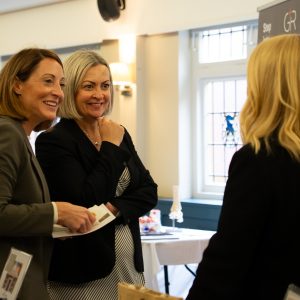 Business people talking at the Visit Knowle Expo in 2025. Two women are smiling broadly talking to someone with their back to the camera