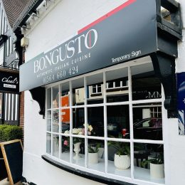 The front of Bon Gusto in Knowle. With pretty window frid painted in white, white painted exterior walls and black restaurant sign with white lettering saying Bon Gusto Authentic Italian Cuisine