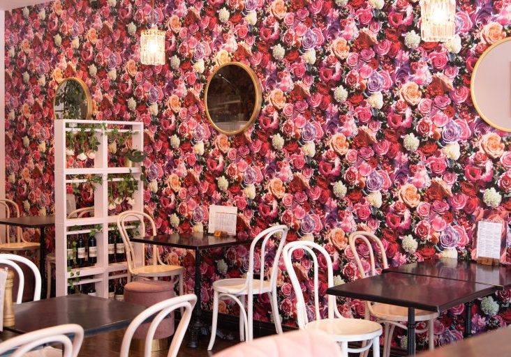 Inside Viola with pink flowery wallpaper and white chairs next to wooden tables