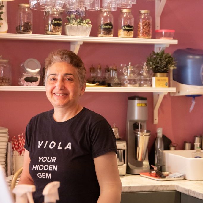 The owner of Viola Bistro is smiling to camera with shelves of coffee behind her